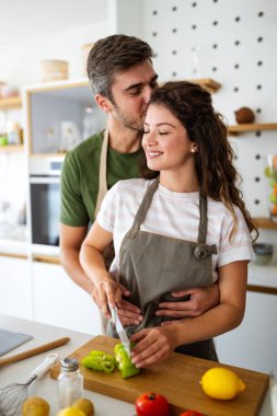 Mutlu genç çift, taze sebze hazırlarken modern mutfakta eğleniyor.