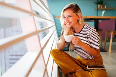 Güzel genç bayan sabahları kahve içiyor. Pencerenin kenarında oturuyor.