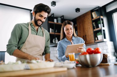 Copule evde mutfakta yemek tarifini internetten izliyor ve birlikte yemek pişiriyor.