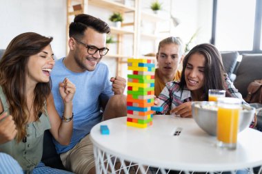 Bir grup genç arkadaş ahşap masa oyunu oynarken eğleniyor. Çok ırklı, neşeli insanlar birlikte eğleniyor ve gülümsüyor.