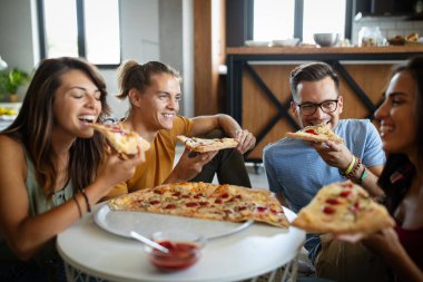 Neşeli çok ırklı arkadaşlar evde pizza yerken eğleniyorlar.