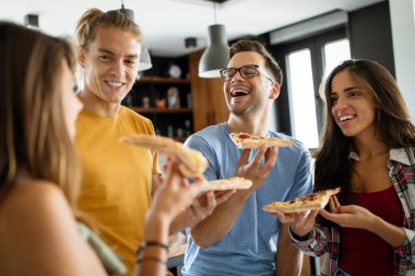 Neşeli çok ırklı arkadaşlar evde pizza yerken eğleniyorlar.