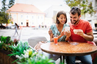 Cep telefonu kullanan, gülümseyen ve kafede konuşan mutlu çift.