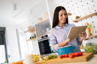 Genç bir kadın evde yemek pişirmeyi internetten öğrenmeye çalışıyor.