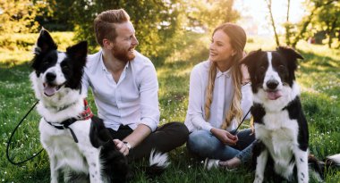 Genç mutlu çift köpeklerle oynuyor, parkta eğleniyor.