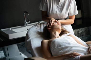 Masör spa salonunda genç kadın vücuduna masaj yapıyor.