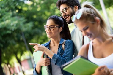 Bir grup arkadaş ya da üniversite öğrencisi gülümsüyor, sınava dışarıda hazırlanıyor.