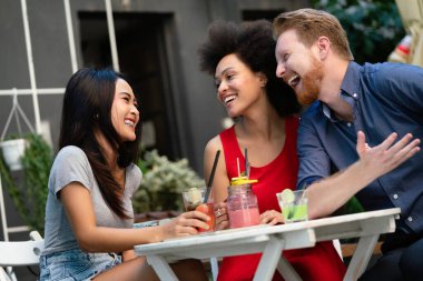 Çeşitli mutlu arkadaşlar yaz aylarında kafede eğleniyor, konuşuyor, gülümsüyor.