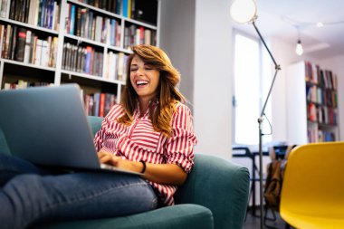 Kanepede otururken dizüstü bilgisayar kullanan mutlu bir kadın.