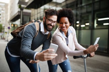 Modern iş binasının önünde elektrikli scooter kullanan iki gülen iş adamı işe devam ediyor..