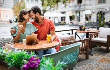 Tablet kullanan, gülümseyen ve kafede konuşan mutlu çift.