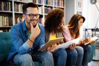 Üniversite öğrencileri kütüphanedeki görevleriyle işbirliği içinde. Kitap okuyan bir grup genç..