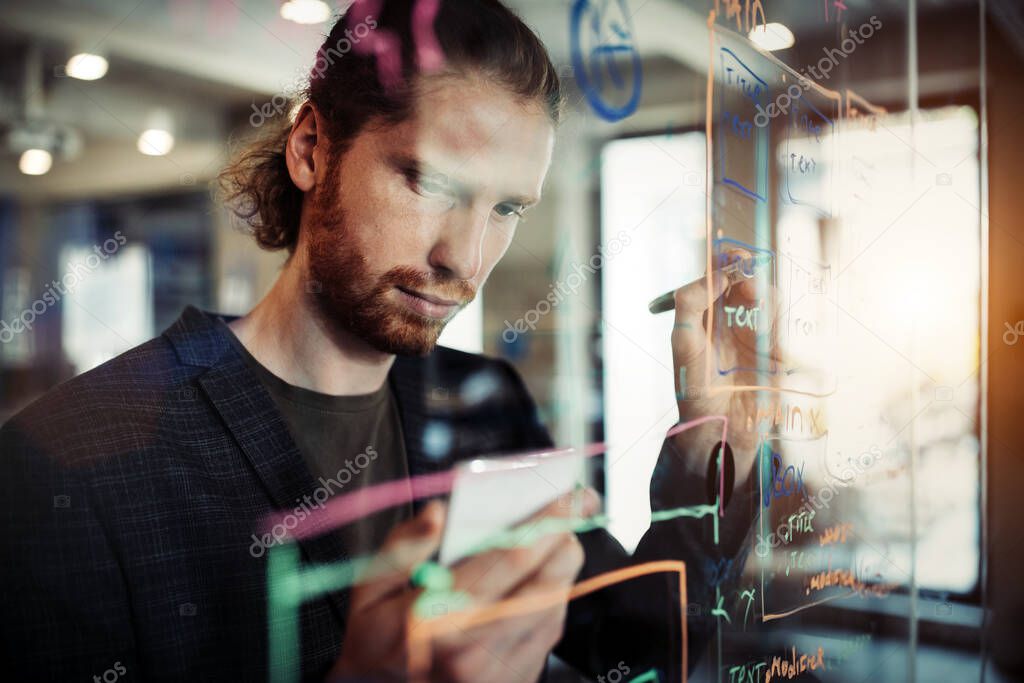 Young man working with datas and diagrams, writing ideas on glass office wall. Business, technology, brainstorming concept.