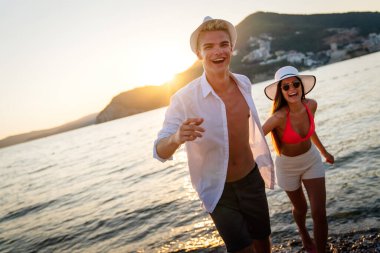 Güzel kumsalda yürüyen, yaz tatilinin tadını çıkaran çekici bir çift.