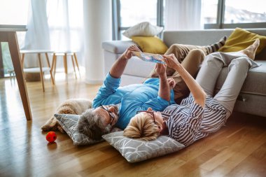 Güzel mutlu son sınıf çifti dijital tablet kullanıyor, evde eğleniyor, gülümsüyor.