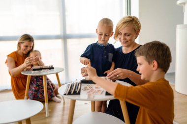 Masadaki genç kadınlar çocuklarla masa oyunu oynuyorlar. Aile, kreş, çocukluk konsepti..