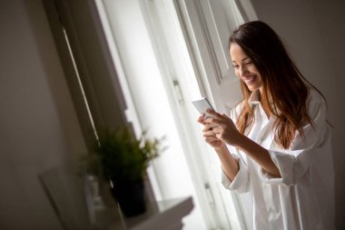 Lüks yatak odasında cep telefonu kullanan tişörtlü güzel bir kadın. İnsanlar, teknoloji, akıllı telefon kavramı