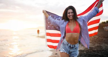 Sahilde neşeli, heyecanlı bir kadın elinde Amerikan bayrağı, eğleniyor..