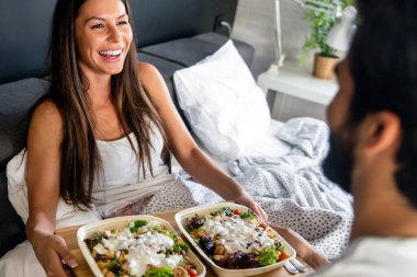 Yatakta rahat ve mutlu bir kadına kahvaltı tepsisi uzatıyorum. Çift, aşk konsepti.