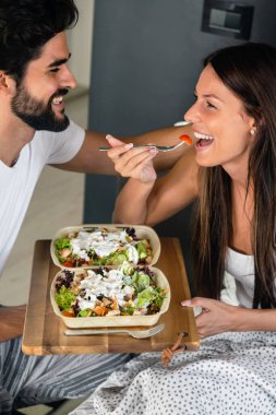 Yatakta rahat ve mutlu bir kadına kahvaltı tepsisi uzatıyorum. Çift aşk konsepti.