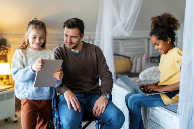 Tekerlekli sandalyede sakat ve evde çocuklarla eğlenen mutlu bir baba. Aile, aşk, teknoloji konsepti