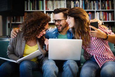 Üniversite öğrencileri kütüphanedeki görevleriyle işbirliği içinde. Kitap okuyan bir grup genç..