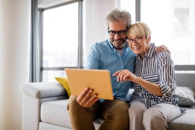 Güzel gülümseyen yaşlı çift evde tablet kullanırken eğleniyor.