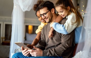 Evde dijital tabletle oynayan çok ırklı kızları olan mutlu bir baba.