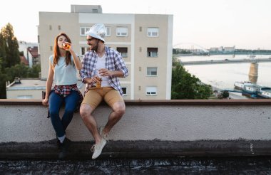 Çiftler gün batımında çatıda içki içerken flört ediyorlar.