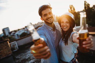 Çiftler gün batımında çatıda içki içerken flört ediyorlar.