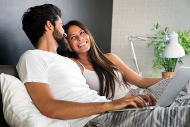 Yatakta dizüstü bilgisayarlı mutlu çift haberleri okuyor ve gülümsüyor.