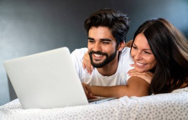 Genç mutlu çift evde yatıp dizüstü bilgisayar kullanıyor..