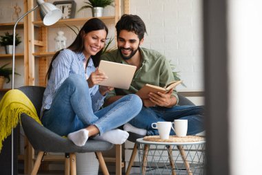 Mutlu genç çift evde dinleniyor. Kitap ve tablet bilgisayarda bir şeyler okunuyor.