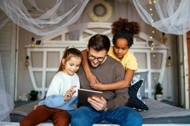 Mutlu çoklu etnik çocuklar ve babalar evde tablet oynayıp eğleniyorlar.