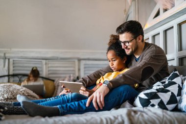 Evde elektronik tablet kullanan çok ırklı baba ve çocuk. Oyun, eğitim, insanlar kavramı