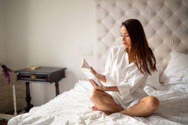 Güzel genç bir kadın hafta sonu evde kitap okuyarak rahatlıyor.