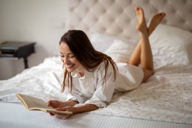 Güzel genç bir kadın hafta sonu evde kitap okuyarak rahatlıyor.