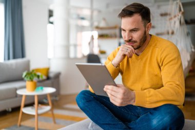 Evde dijital tablet kullanan yakışıklı genç adamın portresi.