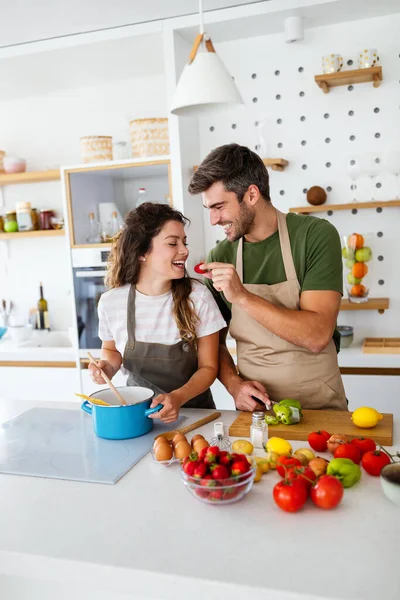 一对快乐的年轻夫妇一边准备新鲜蔬菜食品 一边在现代化的厨房里玩乐 — 图库照片
