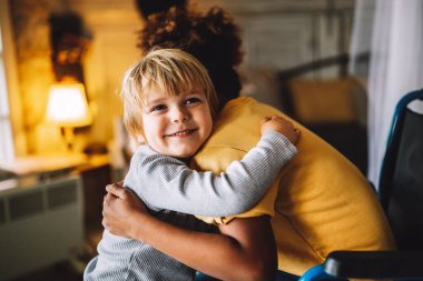 Tekerlekli sandalyedeki engelli küçük zenci kız küçük kardeşine sarılıyor. Engellilik, aile, aşk konsepti