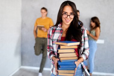 Üniversite hayatının tadını çıkarıyorum. Güzel, mutlu bir kadın elinde kitaplarla arka planda arkadaşlarıyla sohbet ederken gülümsüyor.