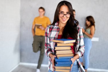 Üniversite hayatının tadını çıkarıyorum. Güzel, mutlu bir kadın elinde kitaplarla arka planda arkadaşlarıyla sohbet ederken gülümsüyor.