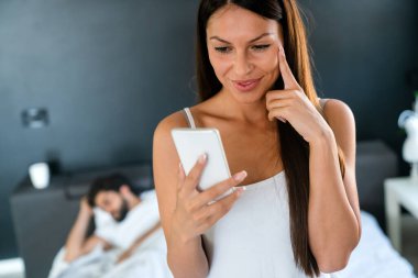 Kocası yatakta uyurken cep telefonuyla konuşan bir kadın. Aldatma, çift, insan konsepti