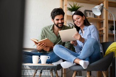 Mutlu genç çift evde dinleniyor. Kitap ve tablet bilgisayarda bir şeyler okunuyor.