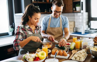 Mutlu genç çift, taze yemek hazırlarken modern mutfakta eğleniyor.