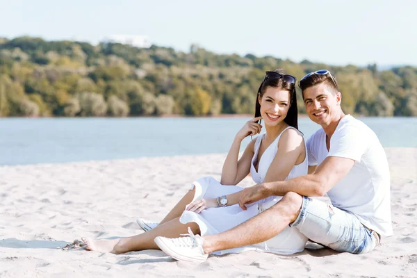 Romantiska unga paret sitter vid en strand — Stockfoto