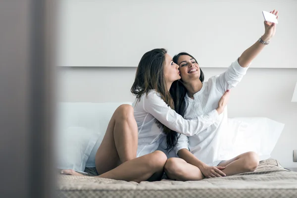 Hot girls lying on a bed taking a photo of themselves — Stock Photo, Image