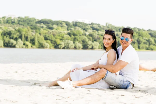 Romantische jonge paar zittend op een strand — Stockfoto