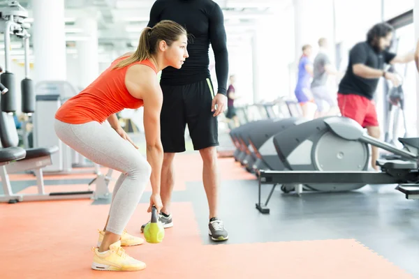 Tainer att ge instruktioner till en kvinna i ett gym — Stockfoto