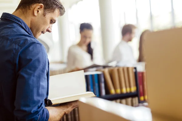 Estudante bonito lendo um livro em uma biblioteca — Fotografia de Stock